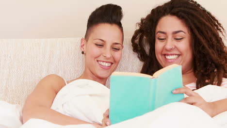 Pareja-De-Lesbianas-Sonriente-Leyendo-Un-Libro-En-La-Cama