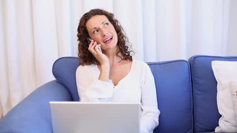 Mujer-Feliz-Usando-Una-Computadora-Portátil-En-El-Sofá-Y-Contestando-El-Teléfono