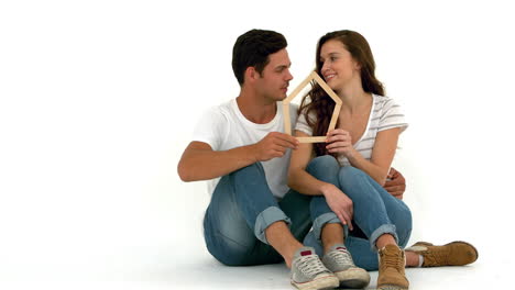 Smiling-couple-sitting-on-the-floor-holding-house-shape