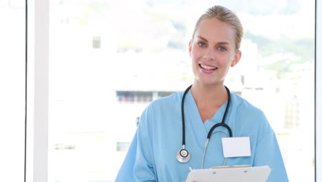 Pretty-nurse-looking-at-camera-and-writing-on-clipboard