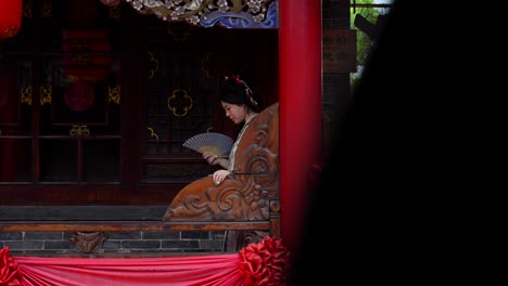 Qing-Dynasty-woman-in-traditional-attire-stands-with-a-hand-fan-on-a-decorated-balcony-in-Pingyao