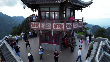 Chinese-woman-waves-from-Liuqi-Pavilion-in-Huangshi-Village-as-drone-lands-and-films,-Zhangjiajie