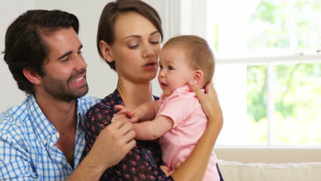 Cute-couple-sitting-on-a-sofa-and-trying-to-calm-their-baby