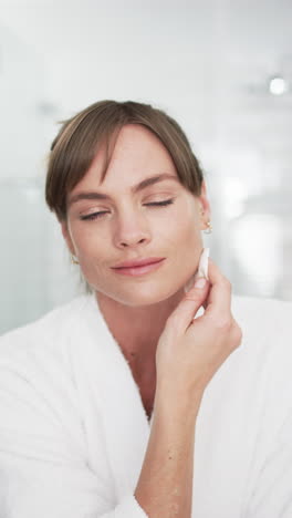 Vertical-video:-Caucasian-woman-in-white-robe-applies-lip-balm-at-home