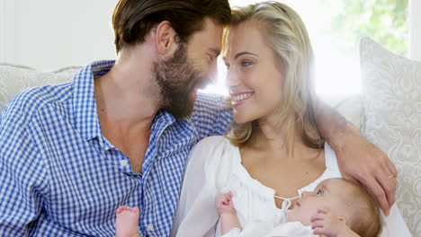 Young-couple-sitting-on-a-sofa-holding-their-baby-