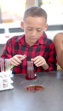 Video-Vertical-De-En-La-Escuela,-Un-Niño-Con-Una-Camisa-A-Cuadros-Roja-Está-Realizando-Un-Experimento-Científico