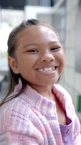 Vertical-video:-In-school,-young-biracial-girl-with-a-bright-smile-is-standing