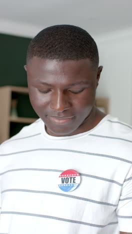 Vertical-video:-Young-African-American-man-in-a-striped-shirt-with-a-voter''s-badge