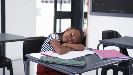 In-a-school,-a-young-biracial-girl-rests-her-head-on-a-desk