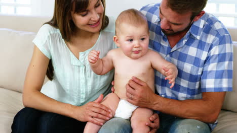 Glückliche-Eltern-Sitzen-Und-Halten-Ihr-Baby-Auf-Dem-Sofa