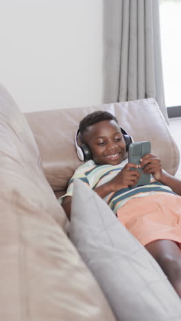 Vertical-video:-African-American-boy-wearing-headphones,-holding-smartphone