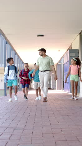 Vertical-video:-In-school,-young-man-holding-hands-with-two-kids-walking