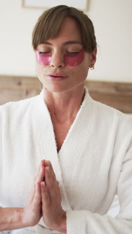 Vertical-video:-Caucasian-woman-in-white-robe-with-pink-eye-masks-at-home