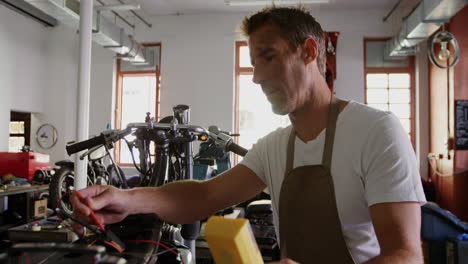 Front-view-of-Caucasian-male-mechanic-checking-battery-of-motorbike-in-repair-garage-4k