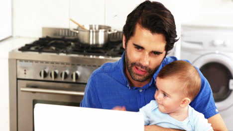 Happy-father-holding-his-baby-and-using-a-laptop