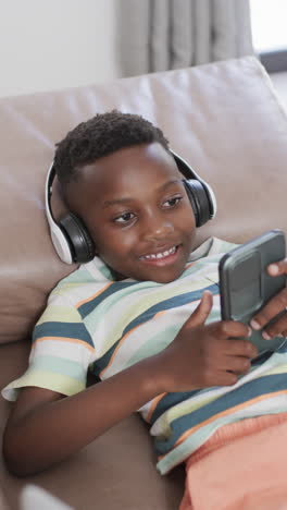 Vertical-video:-African-American-boy-wearing-headphones,-holding-smartphone