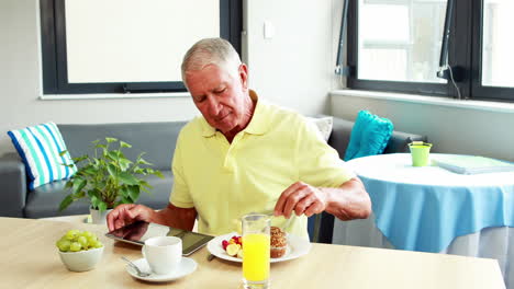 Retired-man-using-tablet-while-eating-breakfast