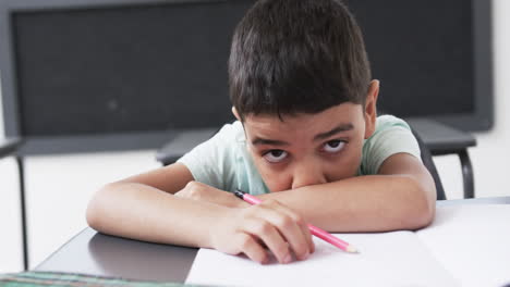 In-a-school-classroom,-a-young-biracial-boy-rests-his-head-on-his-arms