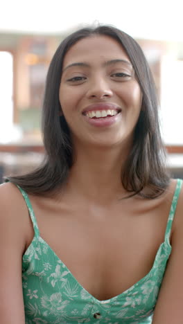 Vertical-video:-A-young-Asian-woman-smiles-warmly,-wearing-a-green-floral-dress