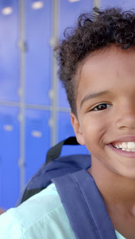 Vertical-video:-In-school,-young-boy-with-a-backpack-standing-by-blue-lockers