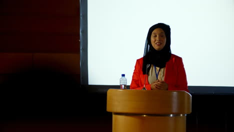 Mature-Caucasian-hijab-businesswoman-speaking-at-podium-in-auditorium-4k