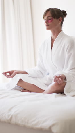 Vertical-video:-Caucasian-woman-meditating-on-bed-at-home