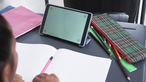 A-young-girl-uses-tablet-with-a-green-background-in-a-classroom,-copy-space