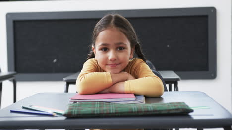 In-a-school-setting,-a-young-Caucasian-girl-rests-her-chin-on-her-hands