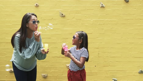 Biracial-mother-and-daughter-in-sunglasses-blowing-bubbles