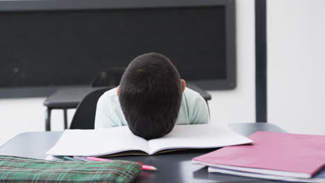 In-a-school-classroom,-a-young-Caucasian-boy-rests-his-head-on-a-desk