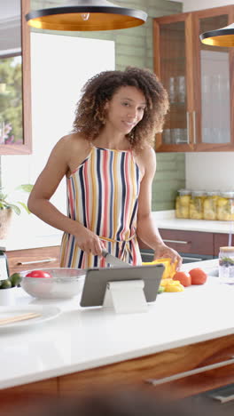 Vertical-video:-A-young-woman-with-curly-hair-is-using-a-tablet-in-the-kitchen