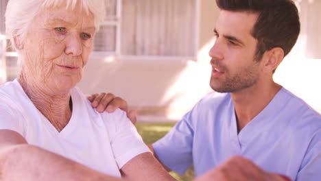 Male-nurse-assisting-senior-woman-to-exercise-in-the-backyard