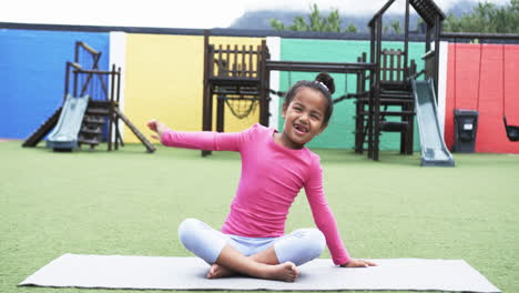 In-a-school-playground,-a-young-African-American-girl-is-seated-on-a-mat