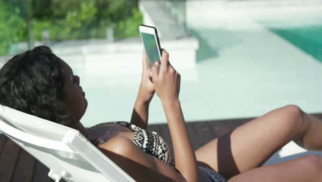 Attractive-woman-lying-on-deck-chair-using-smartphone