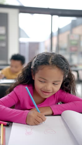 Vertical-video:-In-school,-young-biracial-girl-with-light-brown-skin-is-drawing