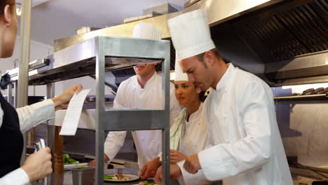 Group-of-chefs-putting-finishing-touch-and-giving-plate-to-the-waitress