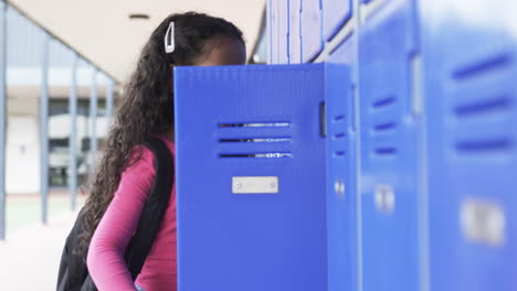 En-El-Pasillo-De-Una-Escuela,-Una-Joven-Afroamericana-Se-Inclina-Hacia-Un-Casillero-Azul