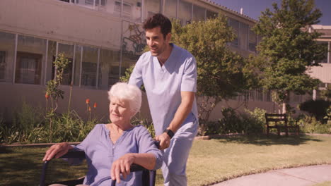 Male-nurse-assisting-senior-woman-on-wheelchair-in-the-backyard