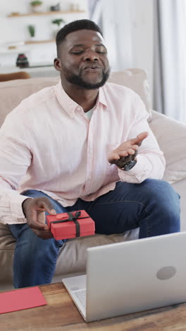 Vertical-video:-African-American-man-holding-gift,-laptop-in-front