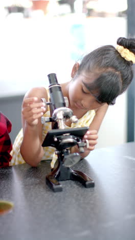 Vertical-video:-In-school,-young-girl-focusing-on-using-a-microscope