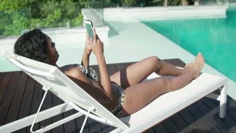 Attractive-woman-lying-on-deck-chair-using-smartphone