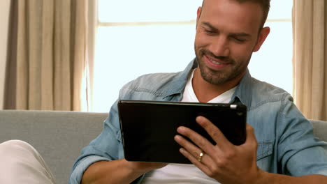 Hombre-Sonriente-Usando-Tableta-En-El-Sofá