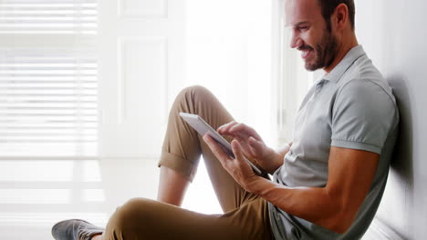 Handsome-man-using-tablet-sitting-on-the-floor