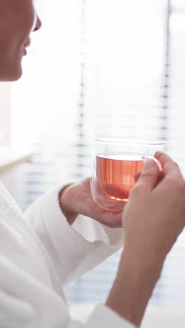 Vertical-video:-Caucasian-woman-holding-clear-mug-with-tea-at-home