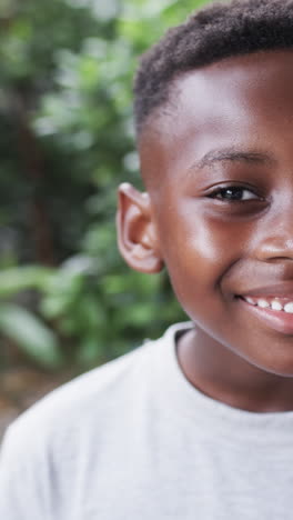 Vertical-video:-African-American-boy-smiling,-green-leaves-background