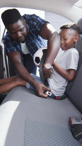 Vertical-video:-African-American-father-securing-son''s-seatbelt,-both-smiling