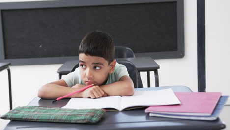 In-a-school-classroom,-a-young-biracial-boy-sits-at-a-desk