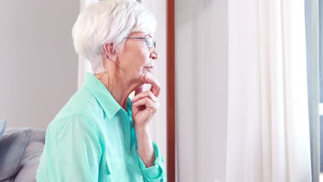 Thoughtful-senior-woman-looking-through-window