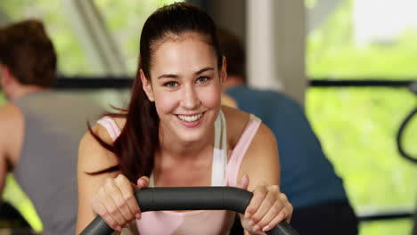 Mujer-En-Forma-Haciendo-Bicicleta-Estática-Sonriendo-A-La-Cámara.