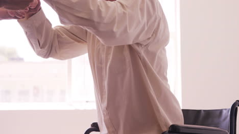 Male-doctor-assisting-senior-man-to-get-up-from-wheelchair